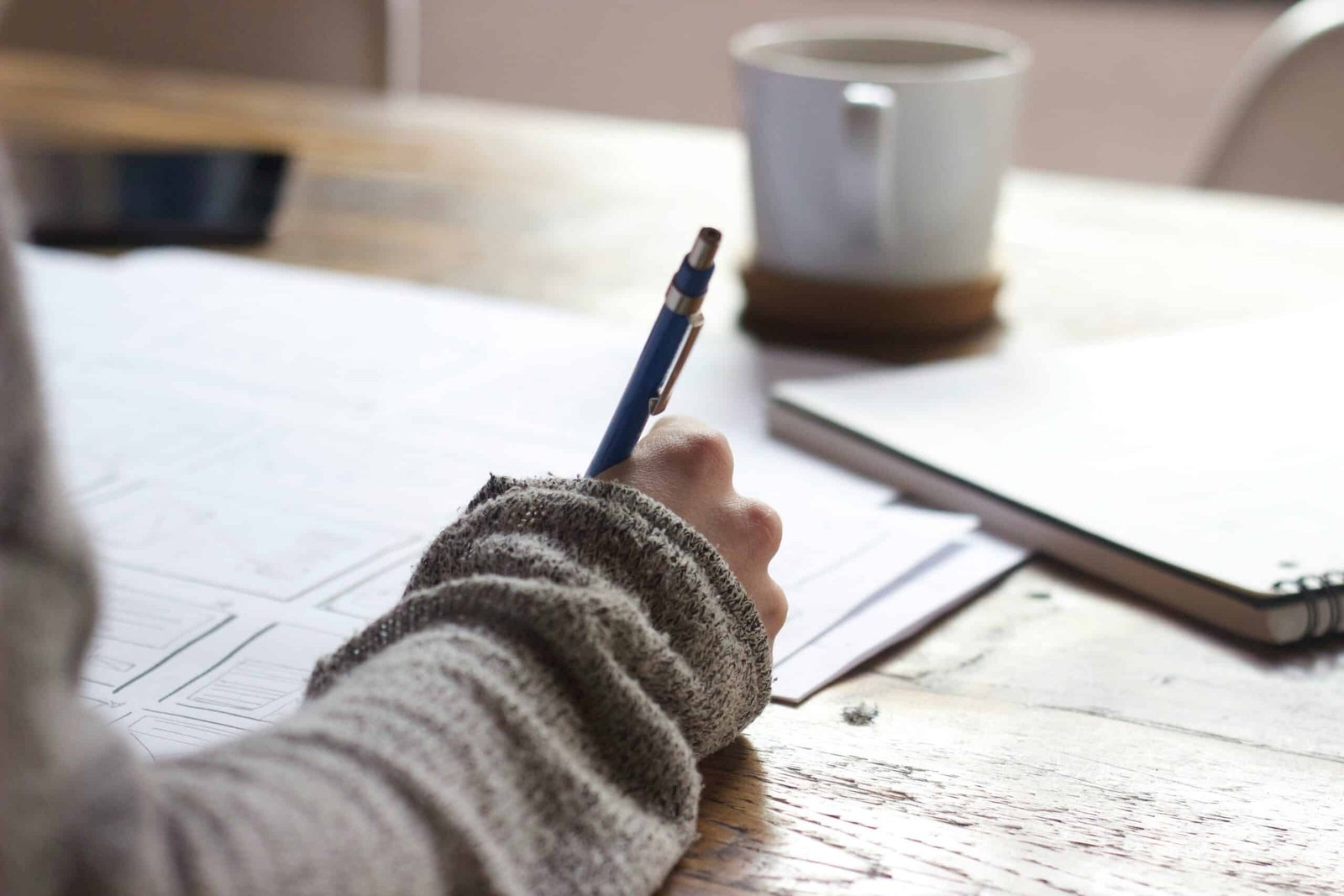 परिश्रम का महत्व person writing on brown wooden table near white ceramic mug