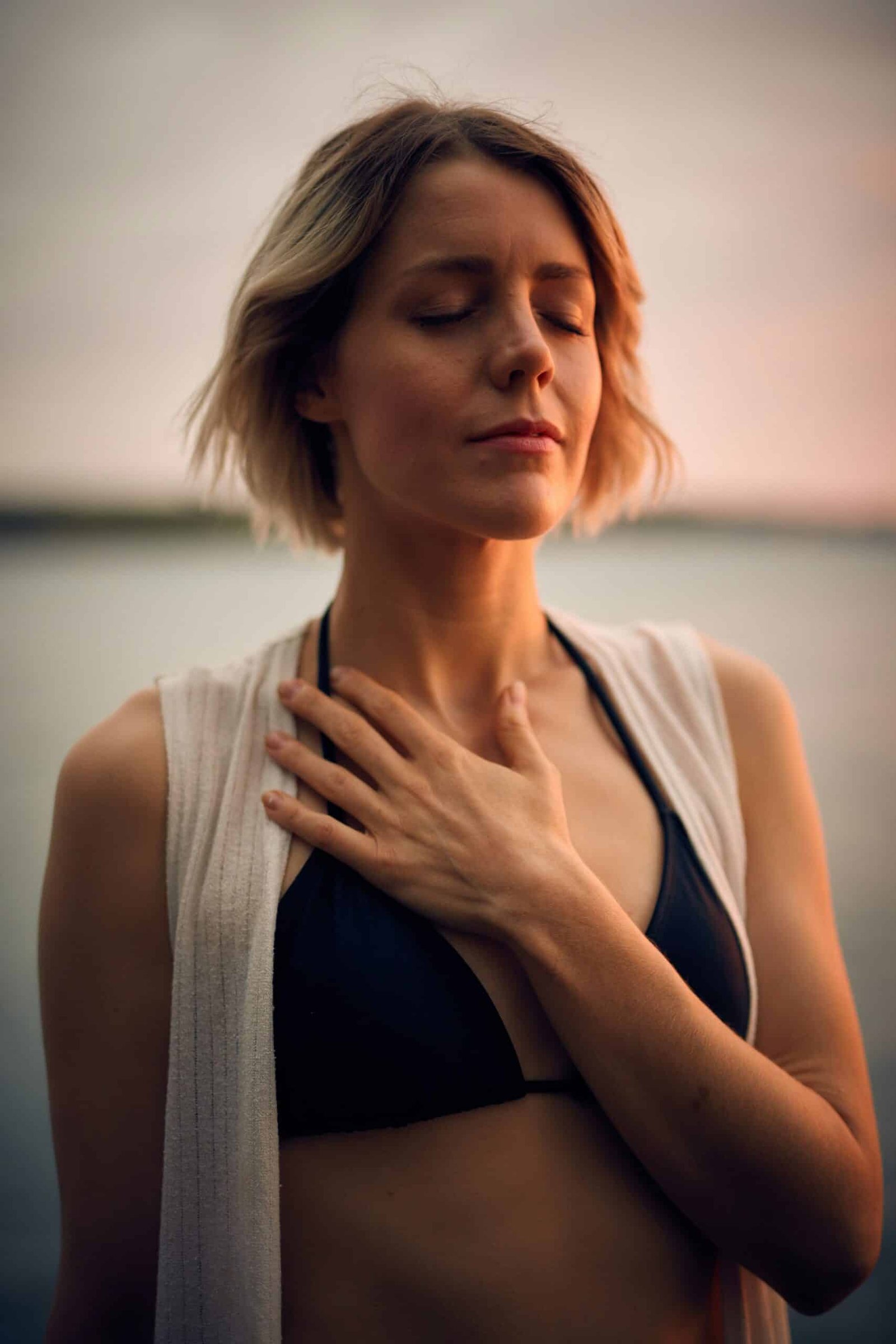 खुश रहने के फायदे woman in white vest and black bikini with hand on chest